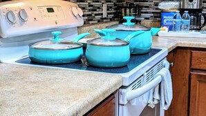 Una cucina con un piano cottura bianco, tre pentole color acquamarina, una macchina da caffè e un erogatore d'acqua sul ripiano.