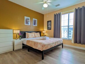 A hotel room with a bed, nightstands, a ceiling fan, and a window with curtains. - Kingsize 3BR Fast Wifi Free Parking Near Disney/Universal. (Kissimmee)