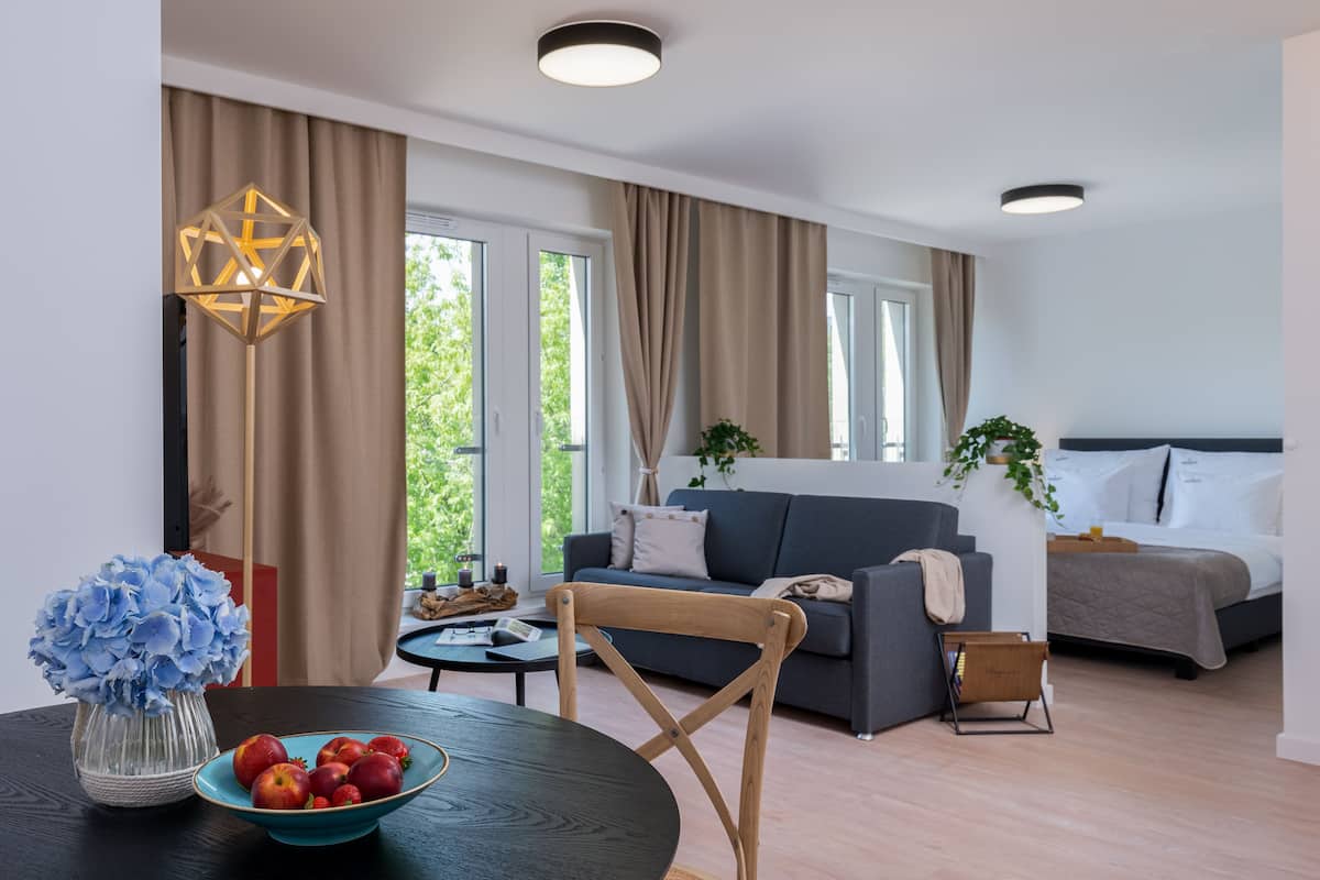Un salon moderne avec un canapé, une table à manger sur laquelle se trouve un saladier de fruits, et un lit avec une tête de lit.