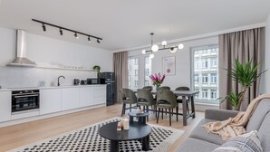 Eine moderne Wohnung mit Küche, Essbereich und Wohnzimmer. Sie verfügt über einen schwarz-weißen Teppich, ein graues Sofa und einen Esstisch mit Stühlen.