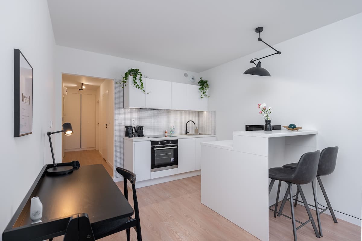 Une cuisine moderne avec des meubles blancs, un plan de travail noir et un petit îlot central doté de deux chaises.