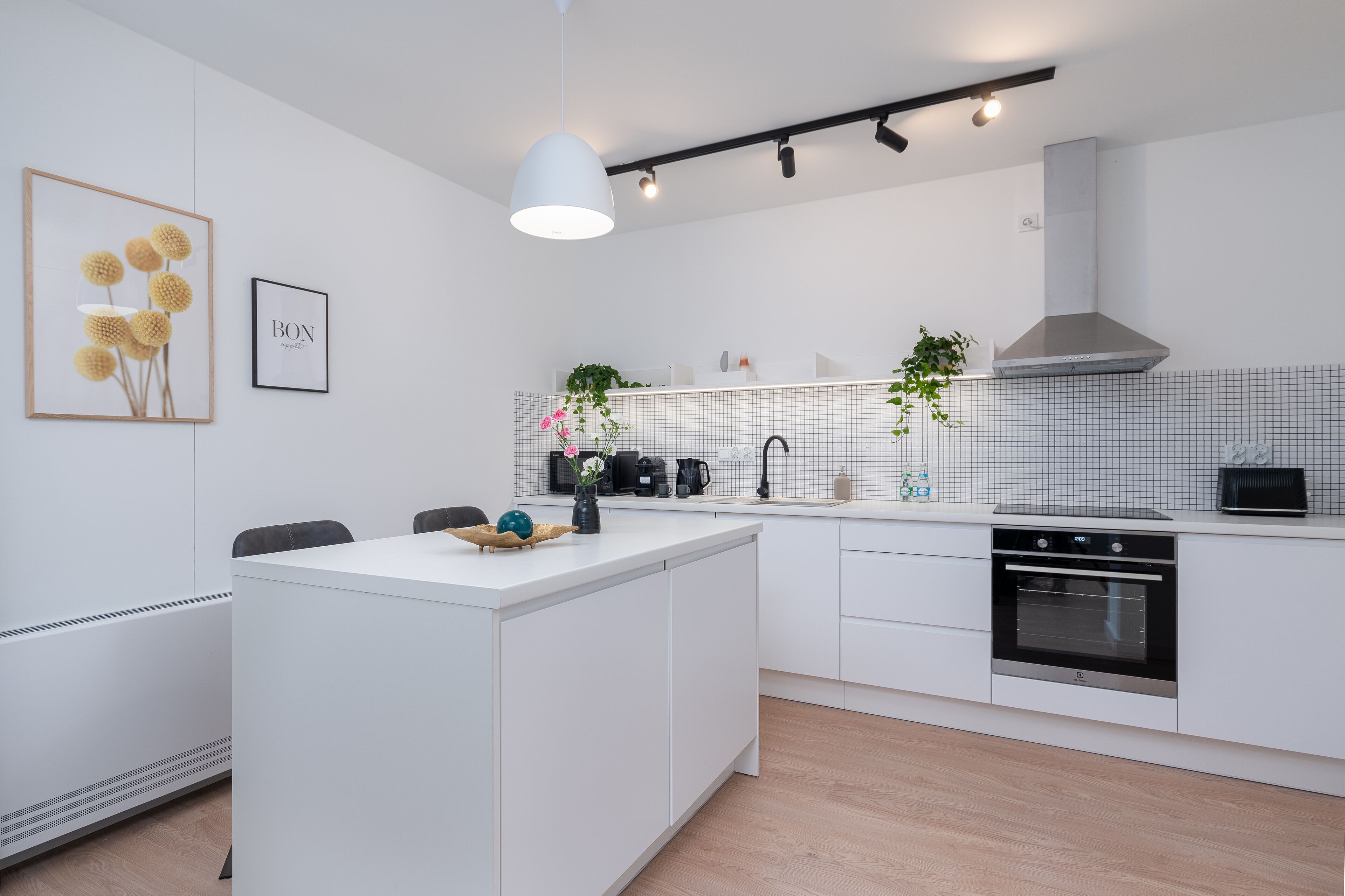 A modern kitchen with white cabinetry, a central island, a built-in oven, and a hanging light fixture.