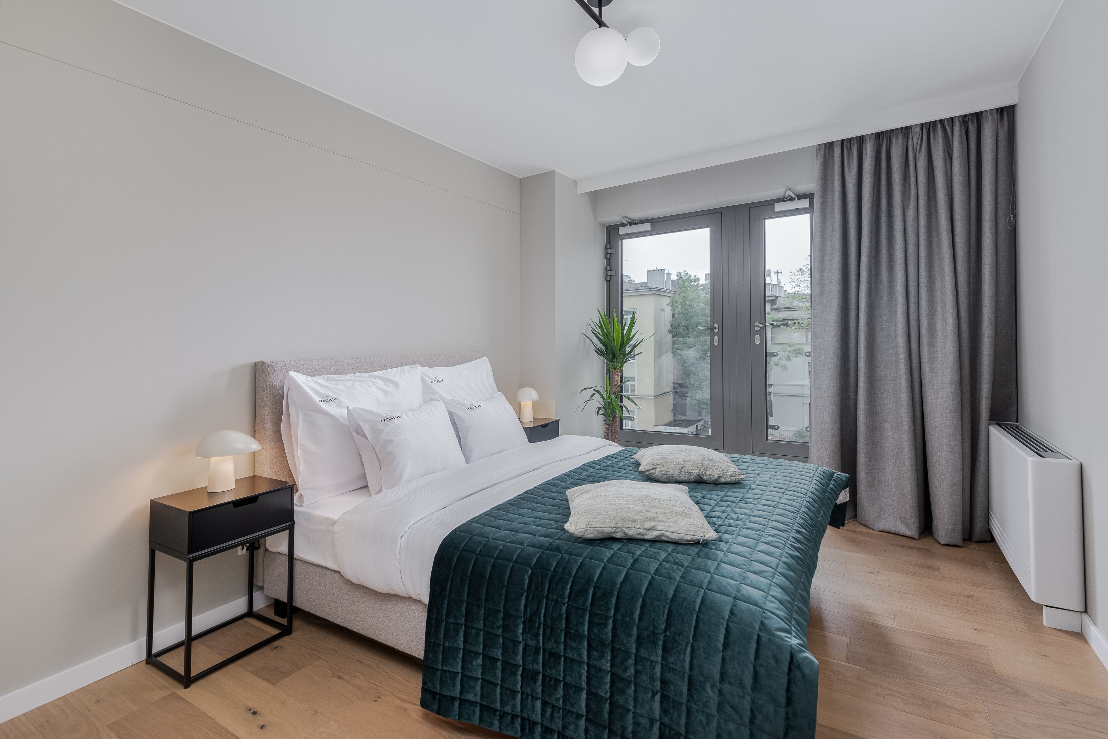 A modern bedroom with a bed, bedside tables, a window with curtains, and a view of the city.