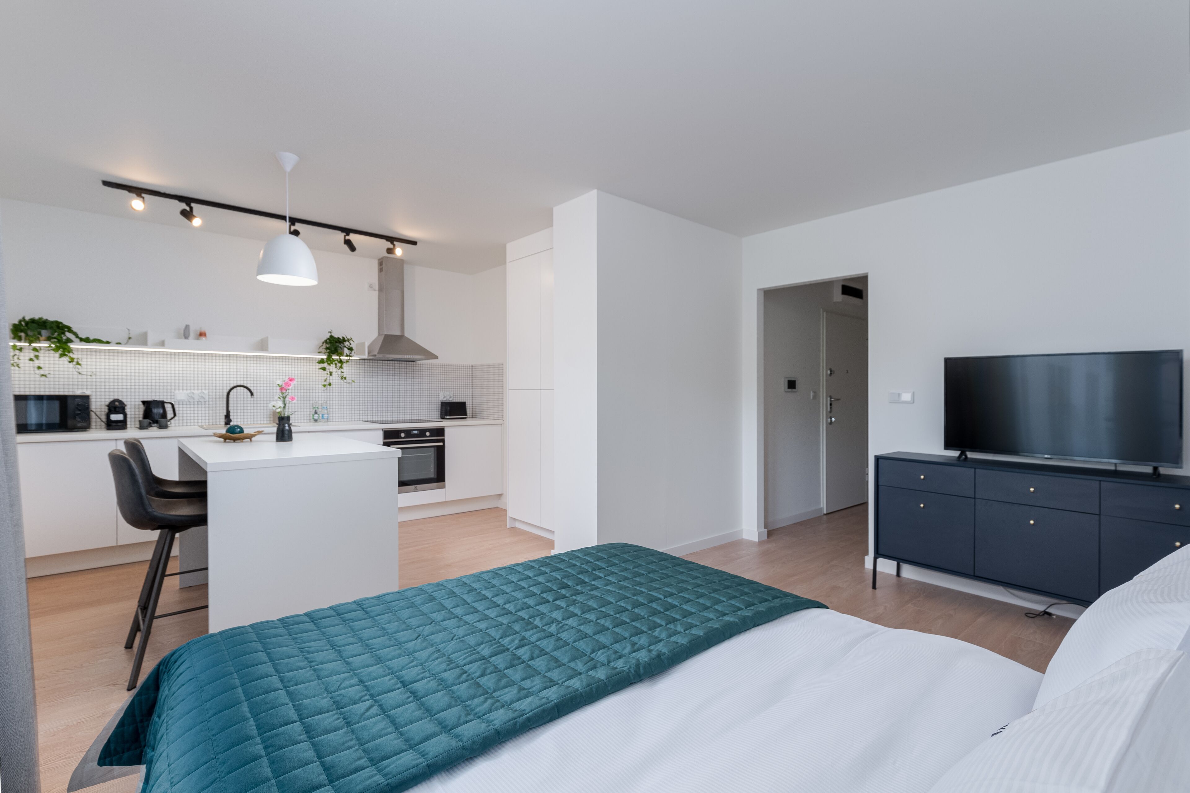 Un apartamento moderno con kitchenette, zona de comedor, un dormitorio con cama grande y televisión.