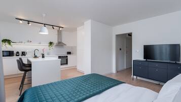 A modern apartment with a kitchenette, a dining area, a bedroom with a large bed, and a TV.