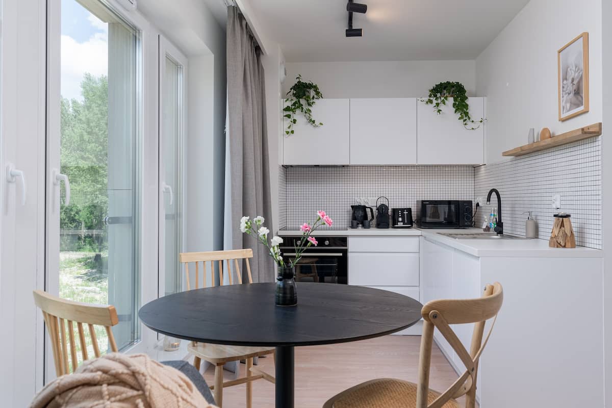 Une cuisine moderne avec des meubles blancs, un plan de travail noir et un coin repas comprenant une table ronde et des chaises.