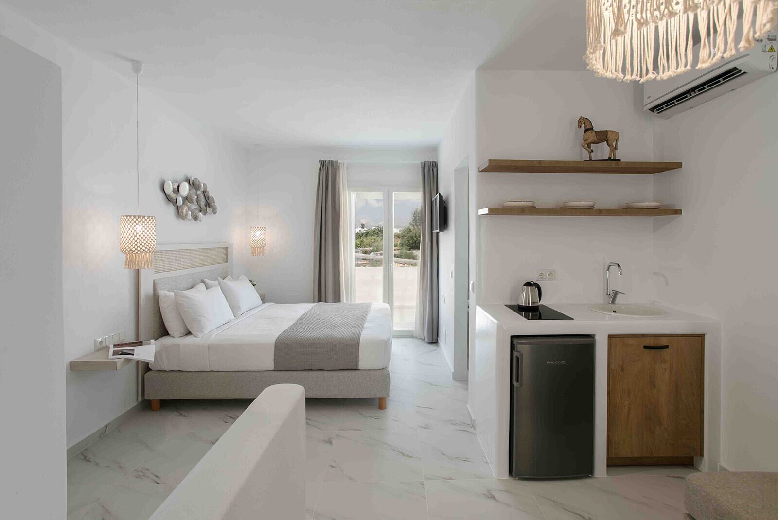 A modern hotel room with a bed, bedside table, lamp, and a view of the outdoors.