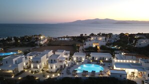 Un resort con piscina, varias edificaciones y vista al mar al atardecer.