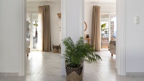 Un pasillo con una maceta tejida, cortinas color beige y vistas a un balcón con mobiliario exterior.