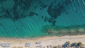 Vista aérea de una playa con agua turquesa cristalina, orilla arenosa y sombrillas dispuestas en filas.