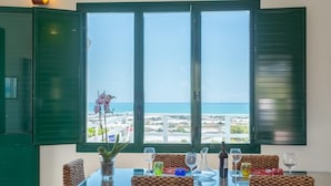 A dining area with a table set for four, a view of the sea, and a potted plant.