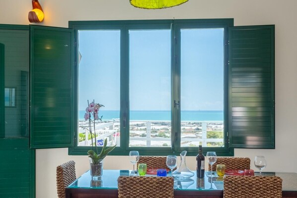 Een eethoek met een tafel voor vier personen, uitzicht op zee en een potplant.