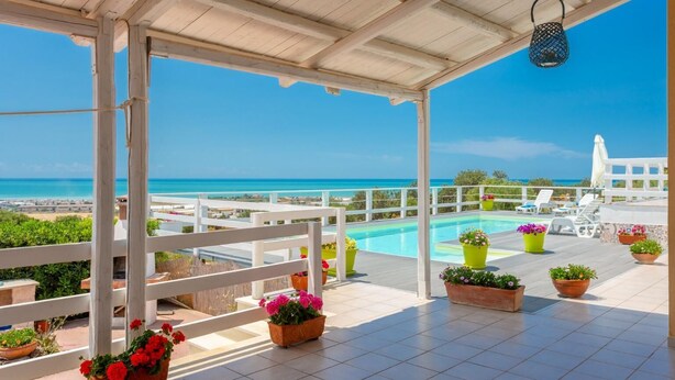 A covered outdoor area with a pool, potted plants, and a view of the sea.