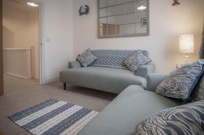 A living room with a grey sofa, patterned cushions, a striped rug, a mirror, and a lamp.