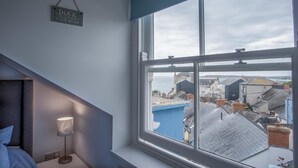A bedroom with a large window overlooking a coastal town. - Ramsey Apartment - 2 Bedroom Apartment - Tenby (Tenby)