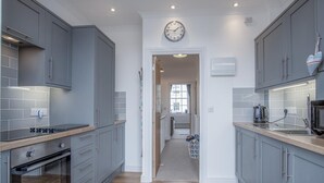 A modern kitchen with grey cabinets, a built-in oven, and a kettle on the countertop. - Ramsey Apartment - 2 Bedroom Apartment - Tenby (Tenby)
