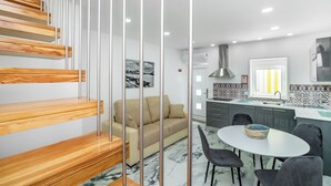 A modern kitchen with a marble floor, a dining area with a round table and chairs, and a staircase with wooden steps and metal railings. - Maredimo Village casa 2 (Porto)