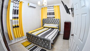 A bedroom with a bed, curtains, a television, and a door. - Apartment in the races near the monument (Santiago De Los Caballeros)
