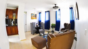 A living room with a brown sofa, a glass coffee table, and a dining area with blue curtains. - Apartment in the races near the monument (Santiago De Los Caballeros)