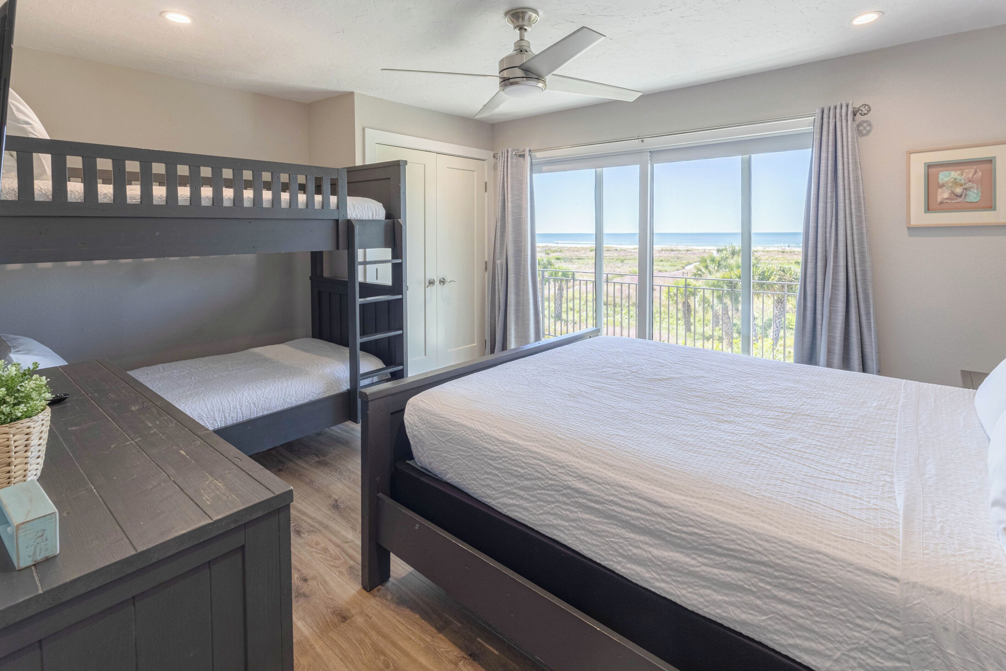 Une chambre avec un lit superposé, un lit simple, un bureau et une fenêtre donnant sur la plage.