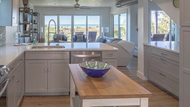 A modern kitchen with a wooden island, a large window overlooking the beach, and a dining area with a view.