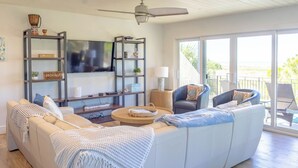 A modern living room with a large sofa, armchairs, a TV, and a bookshelf.