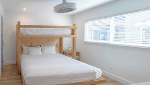 A bunk bed with a wooden headboard, white bedding, and a bedside table with a glass jar.