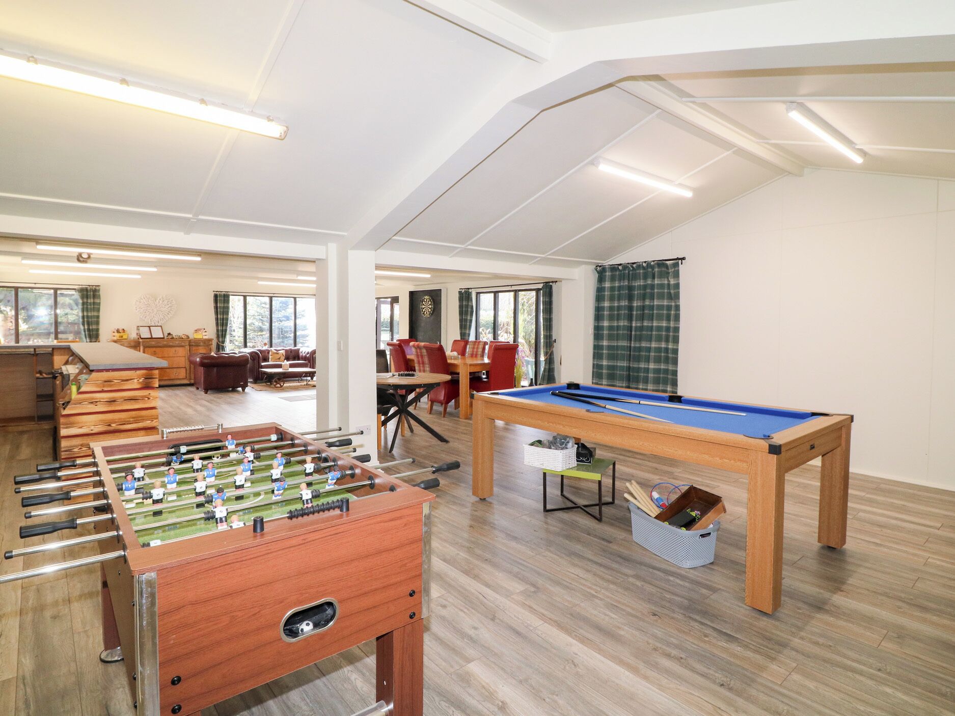 A spacious room with a foosball table, pool table, and a dining area with red chairs.