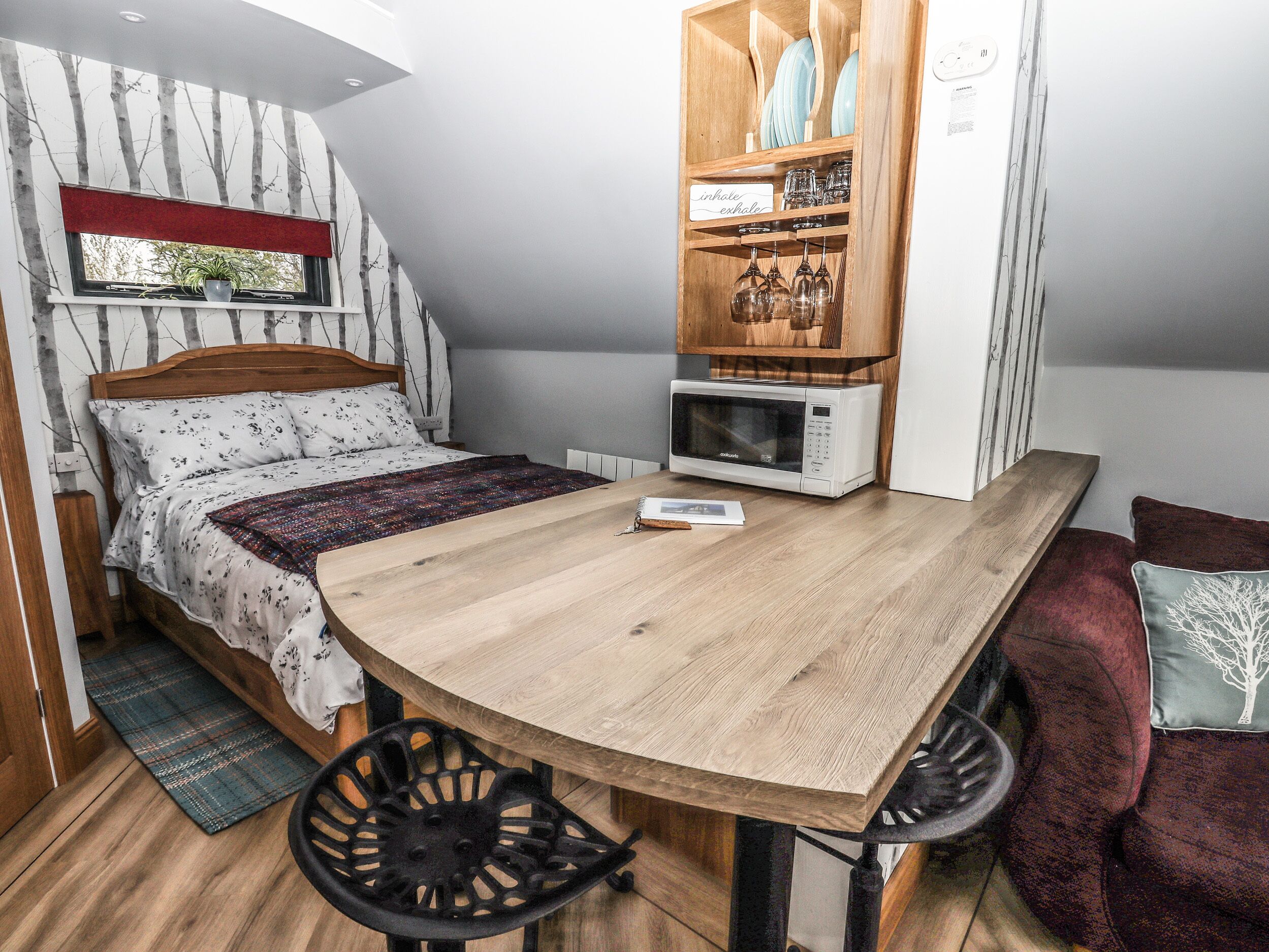 Ein gemütliches Schlafzimmer mit Bett, kleinem Tisch, einer Mikrowelle und einem Schrank mit Geschirr.