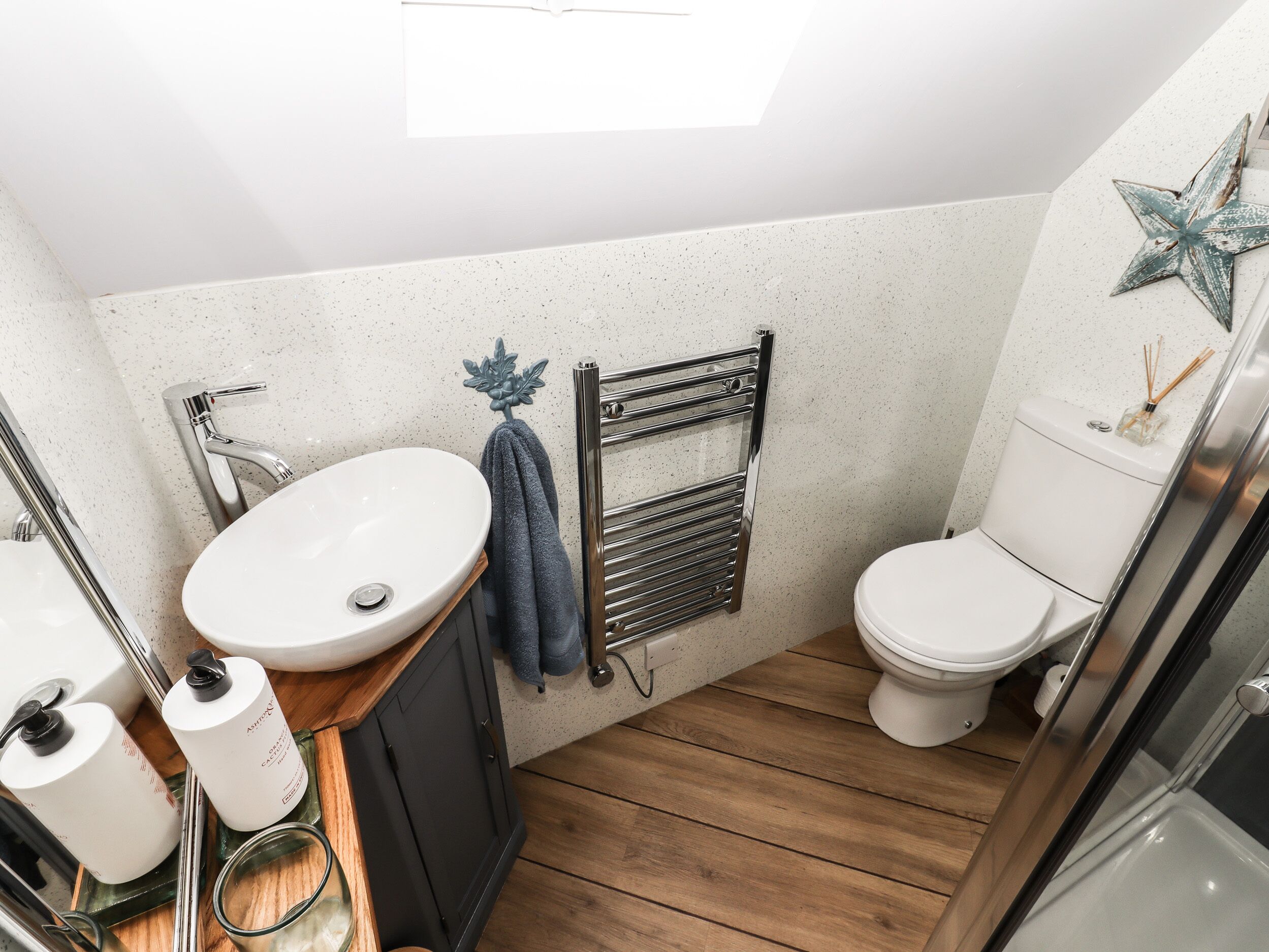 A compact bathroom with a white sink, a toilet, and a wooden floor.