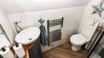 A compact bathroom with a white sink, a toilet, and a wooden floor.