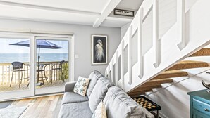 A living room with a grey sofa, a chessboard, and a view of the beach through large sliding glass doors. - Seagrove Villa 11C - Extreme Oceanfront! Resort! (Isle of Palms)