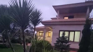 Ein modernes, zweistöckiges Haus mit einem gepflegten Garten, einschließlich Palmen und Sträuchern.