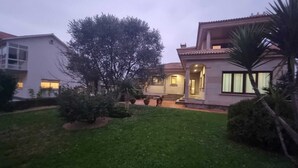 Ein Wohnhaus mit gepflegtem Rasen, einem großen Baum und einer Terrassenanlage mit Stufen zum Eingang.