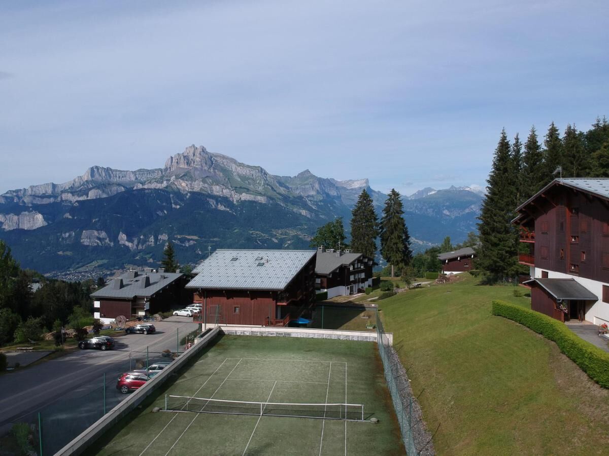 Vue d’une station de montagne avec un court de tennis, des bâtiments et une montagne en arrière-plan.