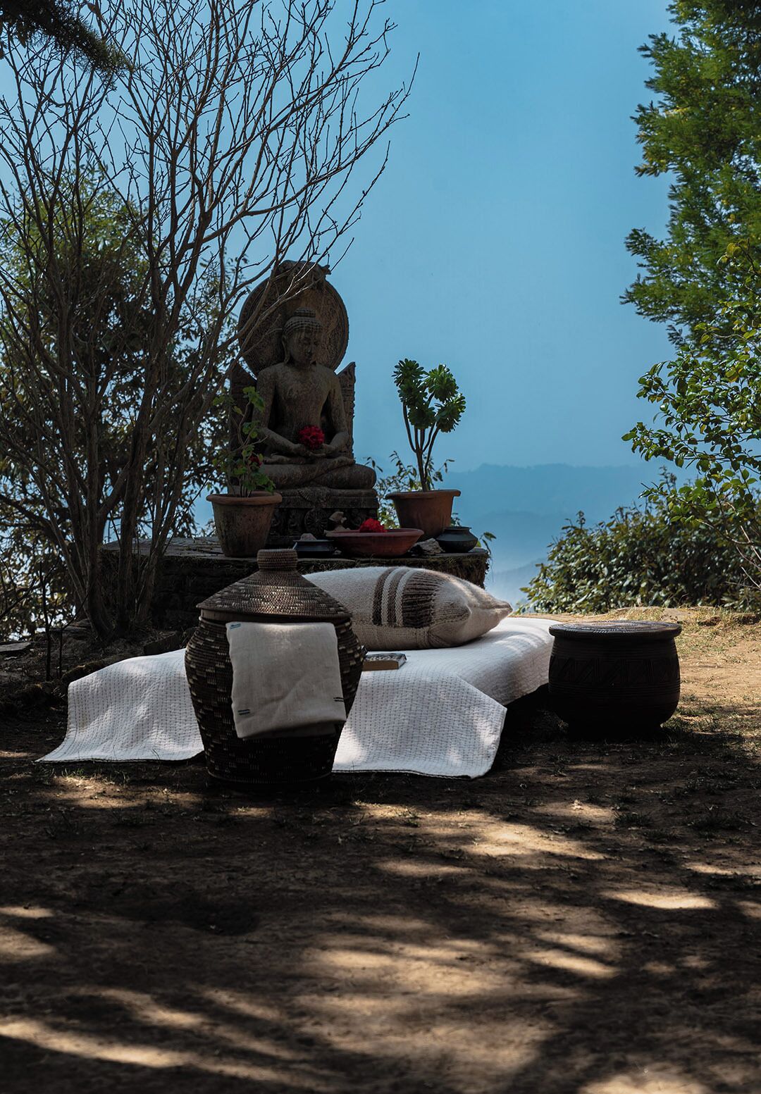 A serene outdoor setting with a Buddha statue, potted plants, and a woven basket on the ground.