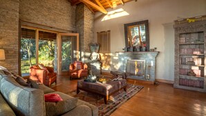 A spacious living room with a stone fireplace, a large bookshelf, and a cozy seating area with a sofa and armchairs. - Mary Budden Estate (Almora)