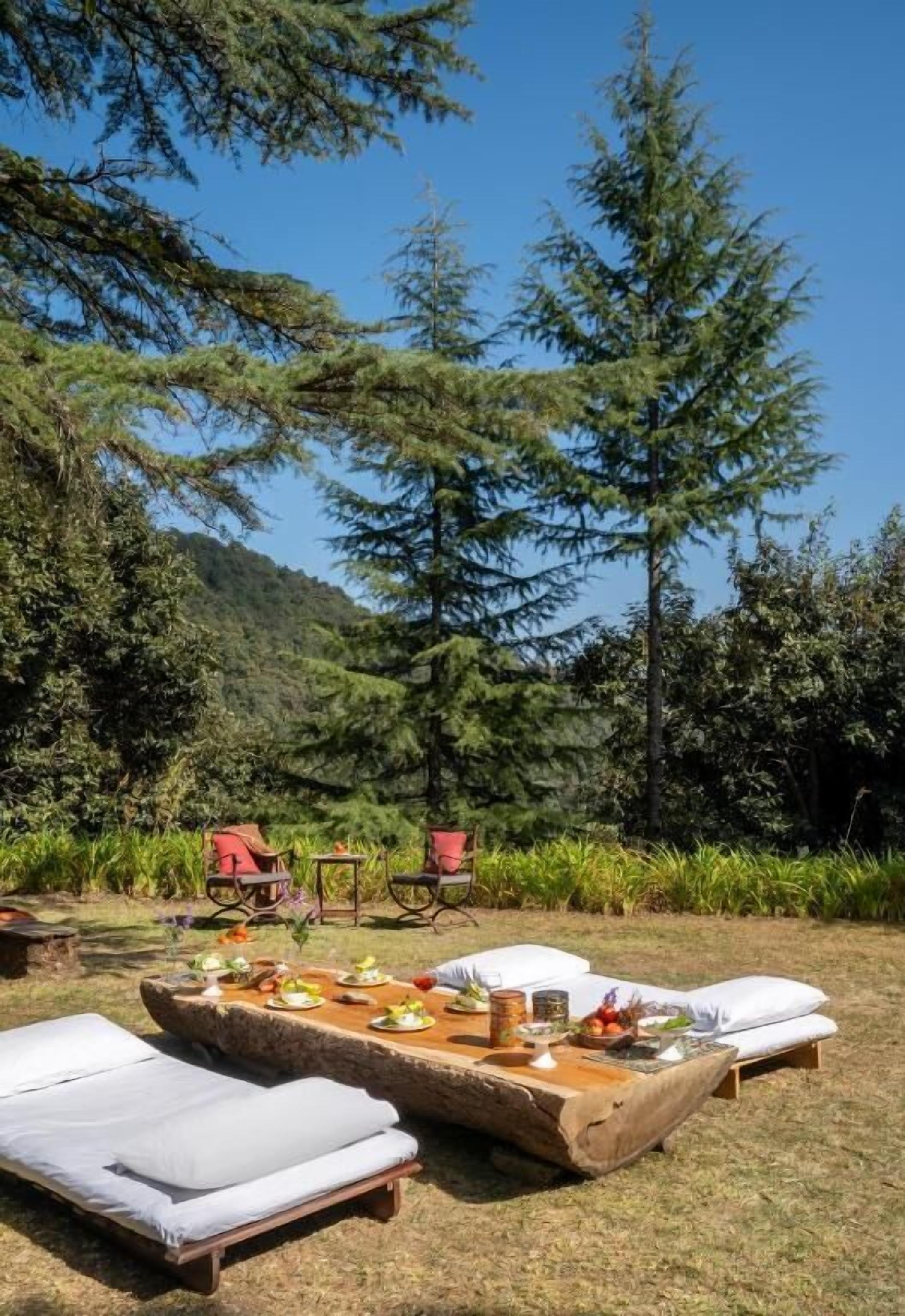 Un área de comedor al aire libre con una mesa de madera lista para una comida, rodeada de sillones y un pintoresco paisaje de montañas.