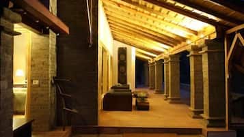Un espace extérieur abrité, doté de murs en pierre et de poutres en bois, qui mène à un espace intérieur aménagé avec des sièges et un escalier.