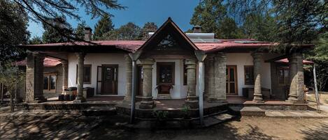 A stone building with a red-tiled roof, featuring a central entrance flanked by columns, and a small porch area with steps leading up to it.