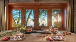 A dining table set for two with a view of trees and mountains through large windows. - Mary Budden Estate (Almora)