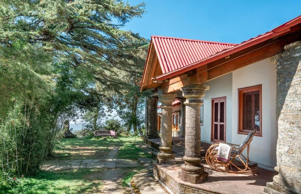 A stone building with a red roof, a covered porch with wooden columns, and a chair outside.