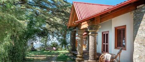 A stone building with a red roof, a covered porch with wooden columns, and a chair outside.