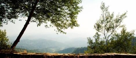 A rustic outdoor setting with a stone table, a book, and a teapot on a grassy area with a view of distant mountains.