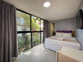 A hotel room with a large window, a bed with white bedding, a bedside table, and a mirror on the wall.