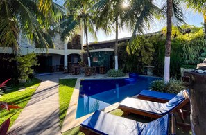 Una piscina con sillas de descanso, rodeada de palmeras y un jardín bien cuidado.