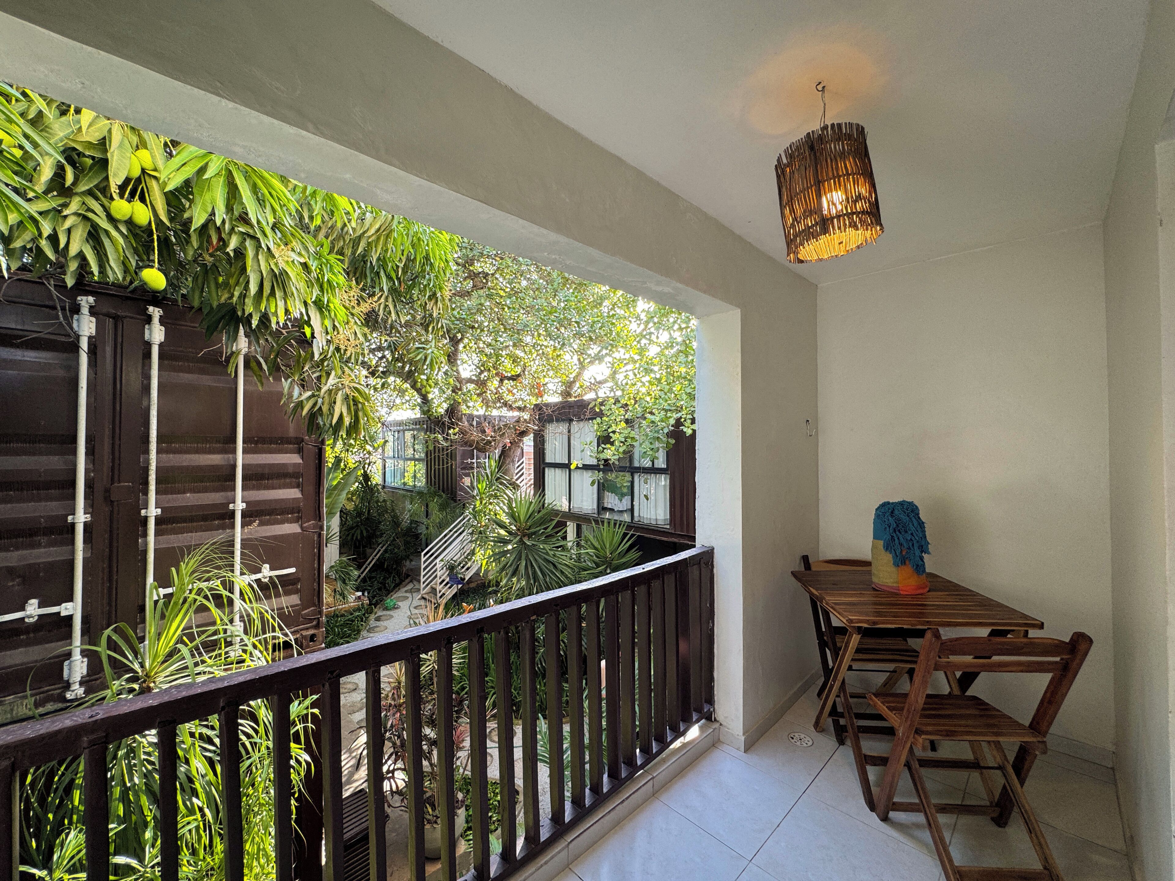 Een balkon met houten hekwerk, een tafel met stoelen en diverse potplanten.