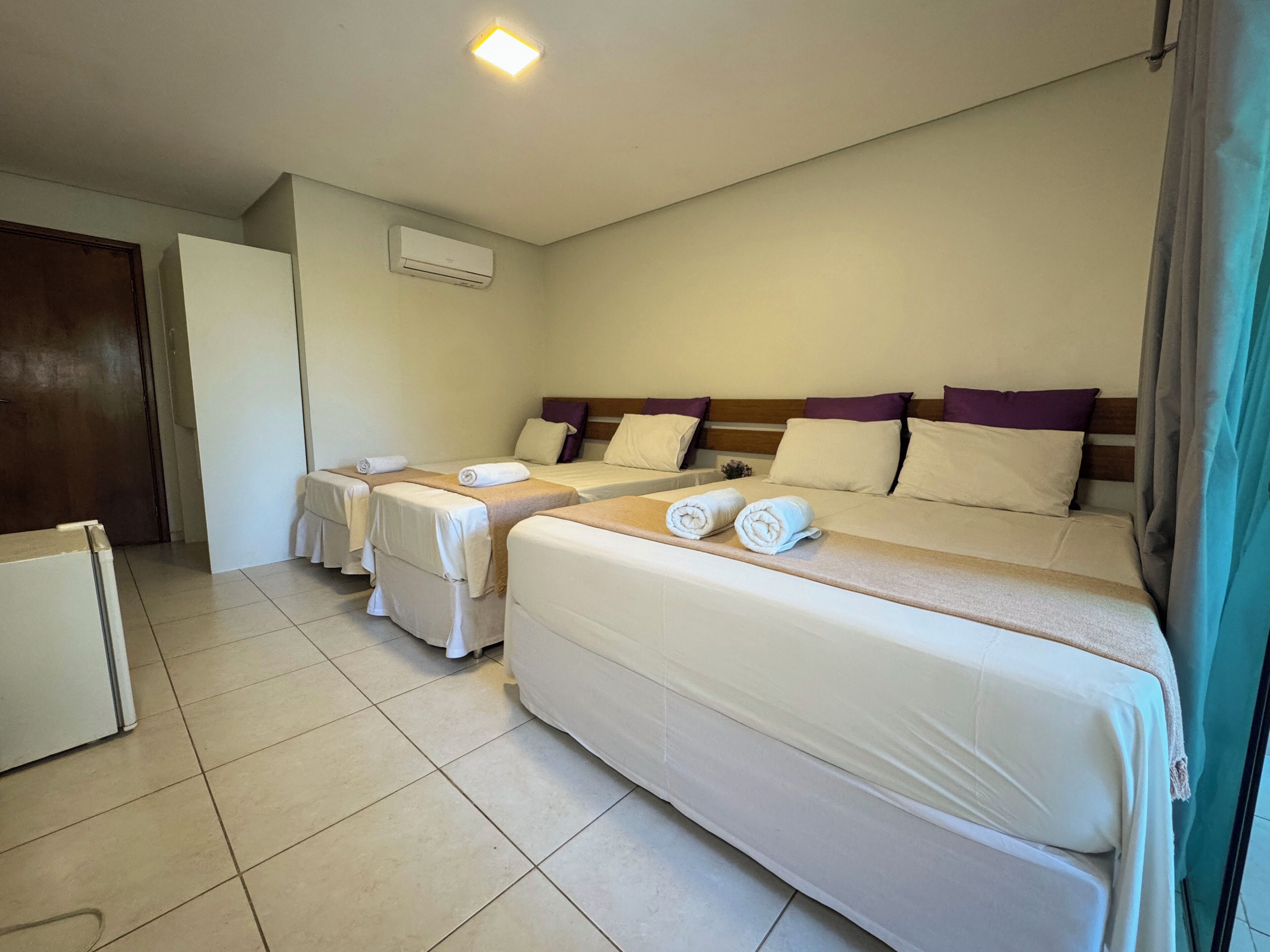 A hotel room with two single beds and a larger bed, all with neatly made linens.
