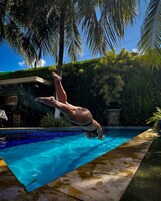 A person diving into a clear blue pool surrounded by lush greenery and palm trees.