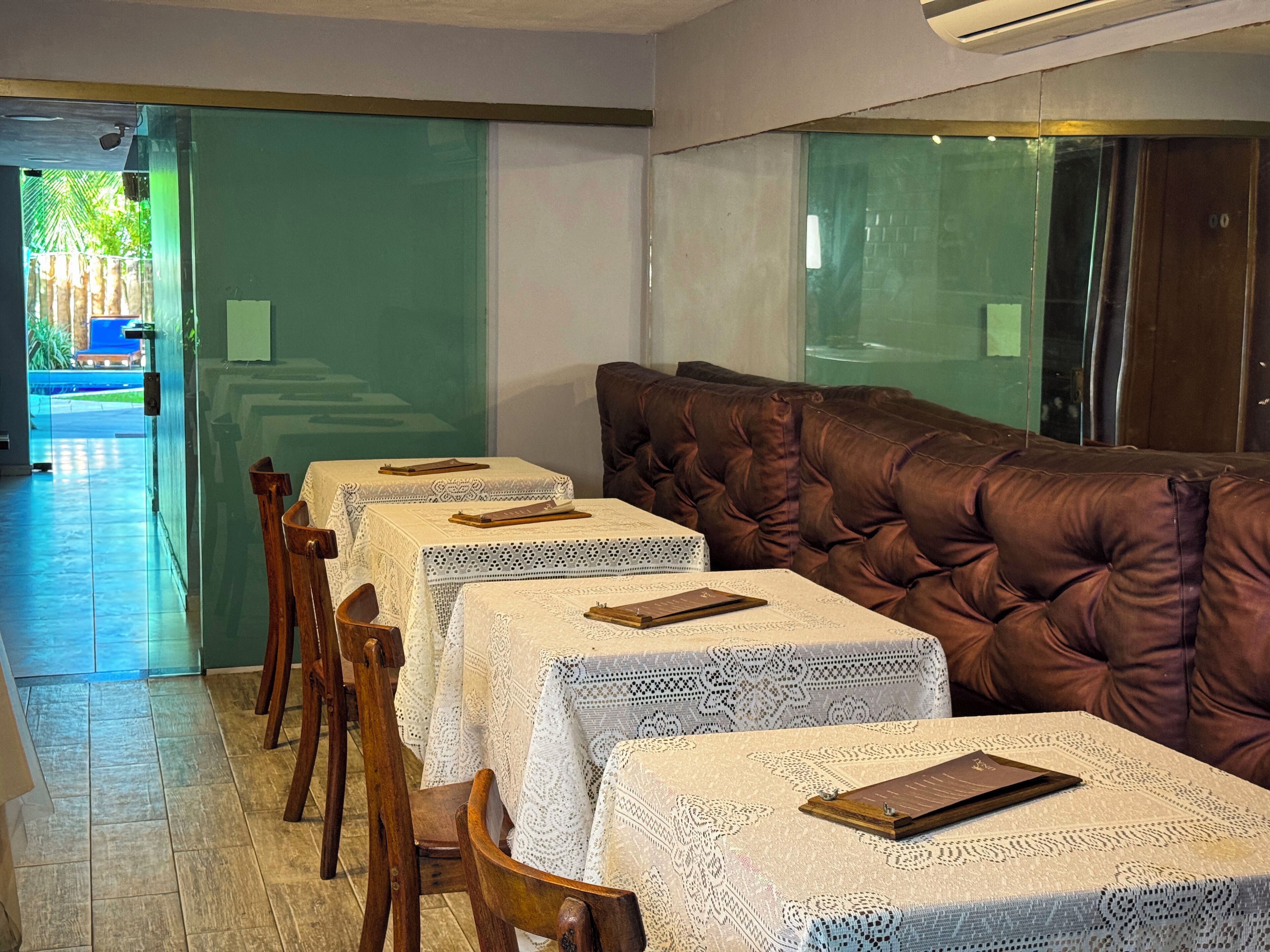 A dining area with tables covered in lace tablecloths, wooden chairs, and a tufted leather couch.